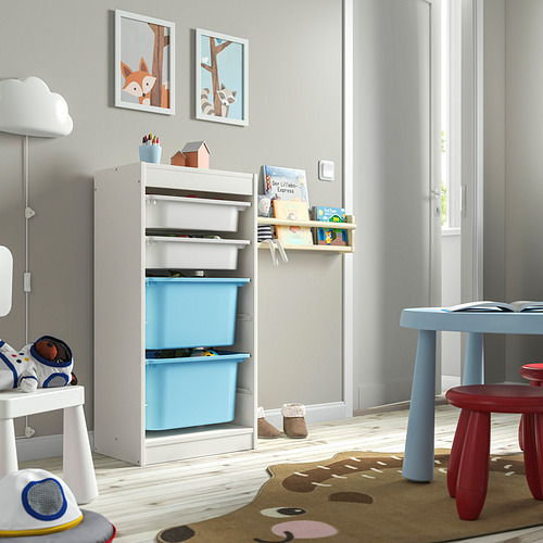 Mueble de almacenaje para niños TROFAST en blanco y azul. Contenedores de plástico, con estructura de madera, bajos y accesibles. Cerca de mesa pequeña, alfombra y juguetes.
