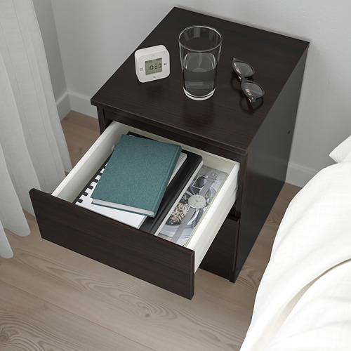 Mesita de noche de madera con cajón abierto con libros y un reloj en la parte superior.