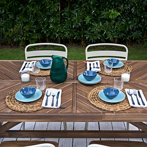 Juego de comedor al aire libre NORRMANSÖ, con capacidad para seis personas con mesa de madera y platos azules.