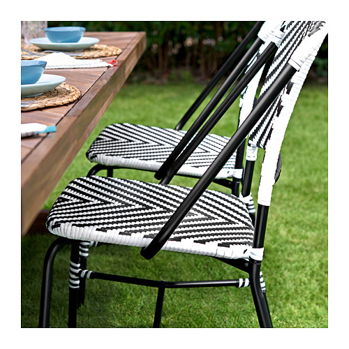 Dos sillas tejidas en blanco y negro junto a una mesa de madera al aire libre con platos y vasos azules.