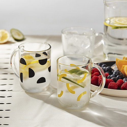 Tres vasos con rodajas de fruta sobre un mantel estampado junto a bayas y rodajas de naranja.