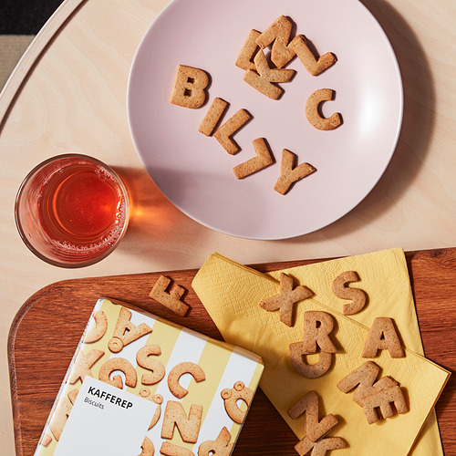 Las galletas del alfabeto deletrean billy en un plato rosa, con una caja amarilla y una bebida en una mesa de madera.