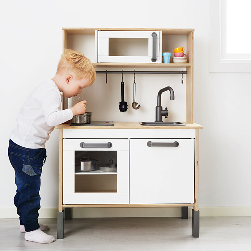 Un niño pequeño finge cocinar en un juego de cocina de juguete, con fregadero, estufa y utensilios.