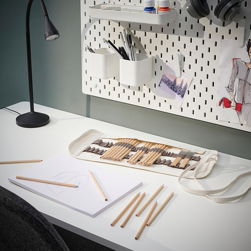 Un escritorio blanco con lápices de colores SOLFÅGEL en un soporte; una lámpara, bocetos y auriculares.