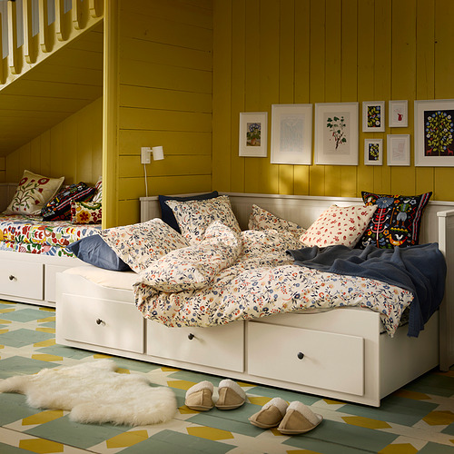 Acogedora habitación con sofá cama floral, paredes mostaza, almohadas estampadas, alfombra y arte.