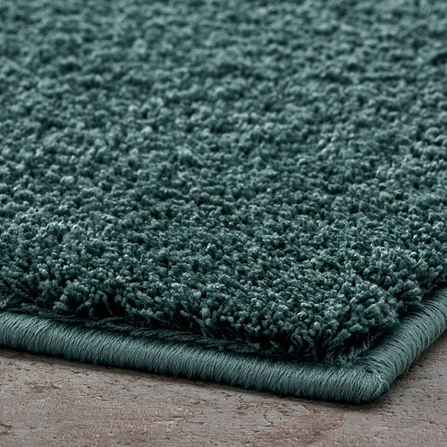 Alfombra de baño verde gruesa y afelpada con una textura suave y esponjosa, probablemente hecha de poliéster reciclado, con un respaldo de látex seguro.