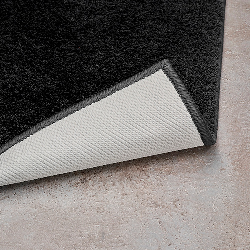 Esquina de la alfombrilla de baño negra con respaldo de látex blanco, que muestra un pelo suave y un agarre seguro.