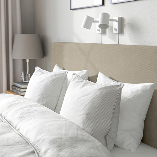 Cama moderna con cabecera suave y acolchada, apliques ajustables, ropa de cama blanca cuidada y un ambiente acogedor y limpio.