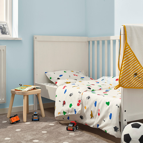Habitación azul brillante con cama infantil blanca y edredón de colores, junto a un taburete y estante estrecho, maximizando eficientemente el espacio.