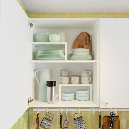 Mueble de cocina con platos verdes, tazas, tazones y tablas de cortar de madera. Estantes blancos, bisagras ajustables. Los ganchos inferiores sujetan los utensilios de cocina.