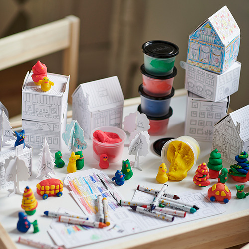 Escena lúdica con set de manualidades MÅLA. Casas en miniatura, arcilla de colores y marcadores sobre la mesa.