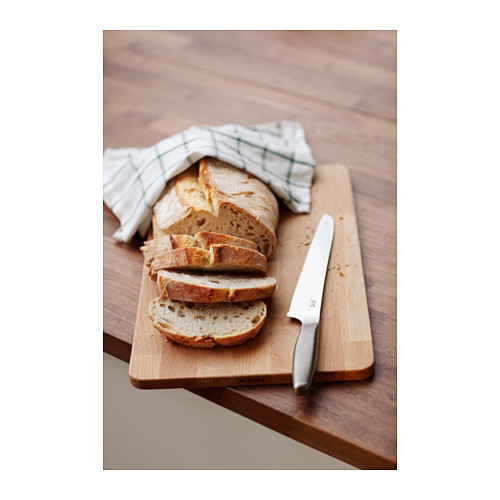 Cuchillo de pan sobre tabla de madera con pan de molde y tela.