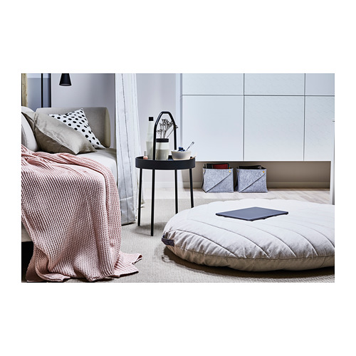 Dormitorio moderno con cama BURVIK, edredón gris, gran cojín en el suelo, pequeña mesa auxiliar redonda con asa, decoración diversa.