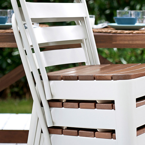 Silla de exterior blanca con asiento de madera, parte del conjunto NORRMANSÖ, robusta y apilable.
