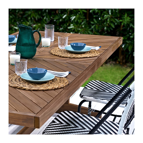 Comedor al aire libre con mesa de madera norrmanso, sillas de mimbre, cuencos azules, vasos y jarra verde.