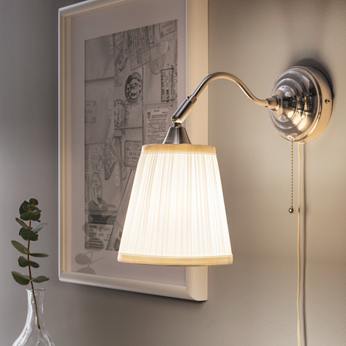 Una lámpara de pared con cuello ajustable y pantalla plisada blanca emite una luz suave junto a una foto enmarcada.