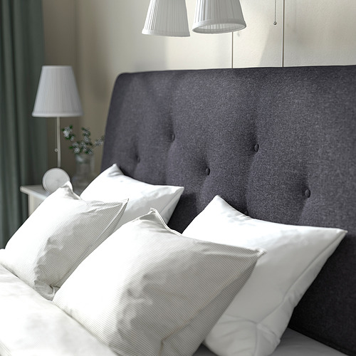 Cama moderna con cabecero gris, almohadas blancas, lámparas y flores.