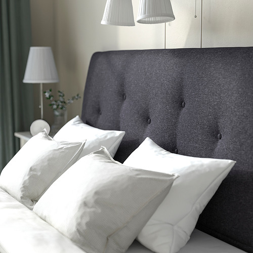 Una cama acogedora con cabecero tapizado en gris, almohadas blancas y lámparas de noche. Ideal para leer y descansar.