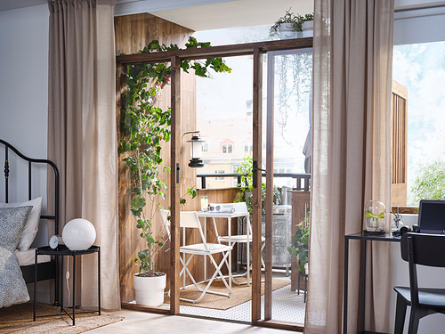 Dormitorio luminoso con balcón, cama, plantas, juego de comedor al aire libre, grandes ventanales.