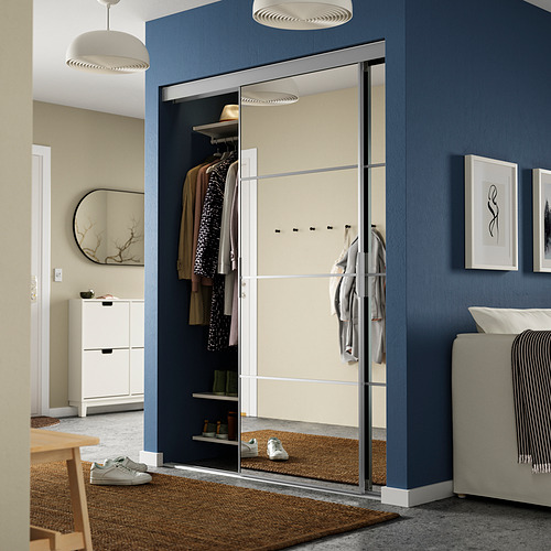 Habitación moderna con armario con espejos SKYTTA, paredes azules, muebles blancos y detalles en madera; Armarios Espejo grande refleja la habitación.