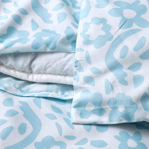 Ropa de cama estampada en azul claro doblada con fondo blanco, probablemente fundas de almohada con cierre de sobre.