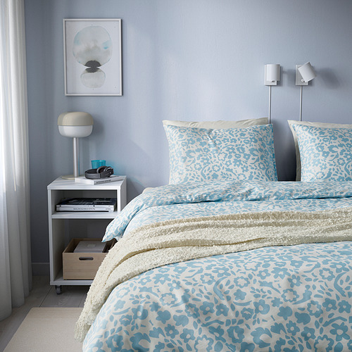 Ropa de cama de flores azules en una acogedora cama blanca, con una moderna mesita de noche cerca.