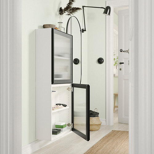 Moderno mueble de almacenamiento BESTÅ blanco con puerta de cristal y bisagras ajustables, decorado con varios artículos.