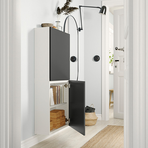Modern white and black ikea BESTÅ storage unit with one door open, displaying books and boxes.