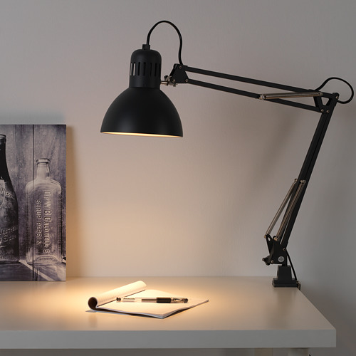 La lámpara de escritorio ajustable negra TERTIAL ilumina un espacio de trabajo con papel y bolígrafo.
