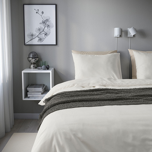 Dormitorio con ropa de cama blanca PILTANDVINGE, poliéster reciclado y viscosa. Paredes grises, decoración minimalista, mesita de noche con libros y lámpara.
