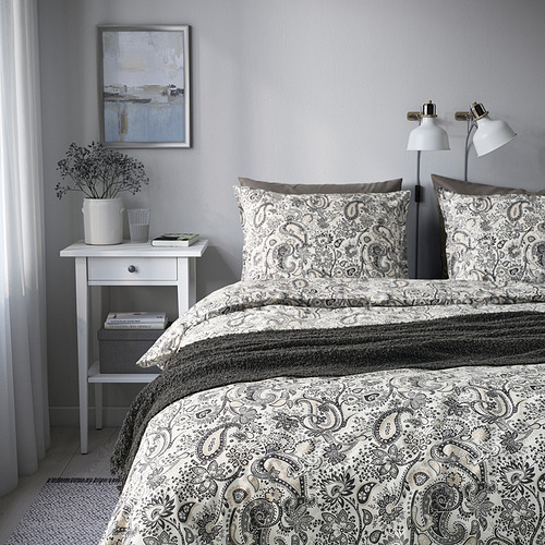 Ropa de cama neutra RODGERSIA ambientada en un acogedor dormitorio, con mesita de noche y obras de arte.