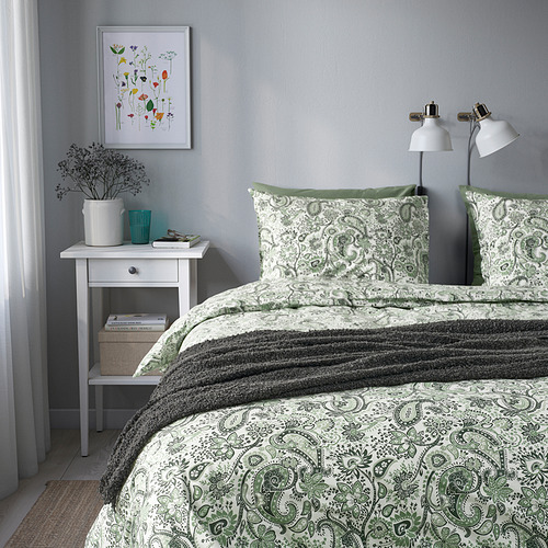 Dormitorio con ropa de cama de cachemira verde, mesita de noche blanca y cuadro en la pared.
