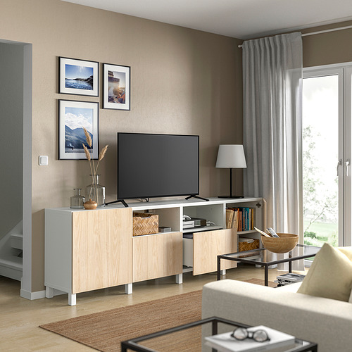Sala de estar moderna con soporte de TV de madera de color claro, televisor de pantalla plana, lámpara cercana y cuadros enmarcados en la pared.