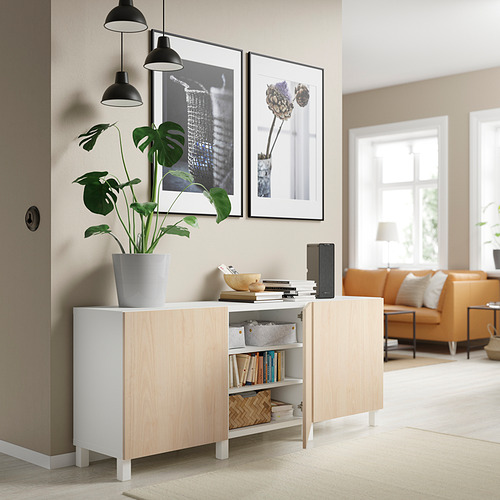 Sala de estar moderna con aparador BESTÅ blanco y madera clara, planta de interior, lámparas colgantes, arte enmarcado y sofá naranja.