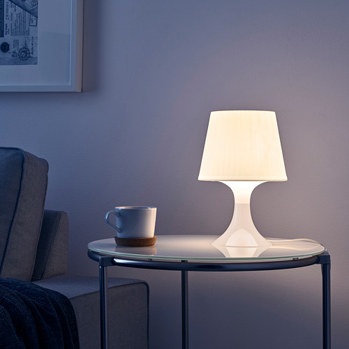 Lámpara LAMPAN en la mesa junto a la taza, que proporciona una luz ambiental cálida y acogedora.