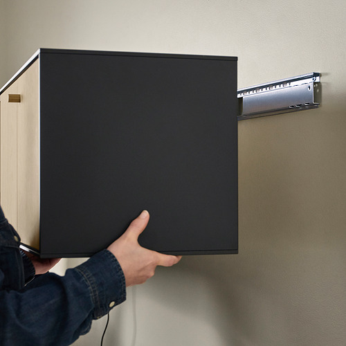 Persona sosteniendo la estantería de pared BOASTAD, preparándose para colgarla con soporte visible.