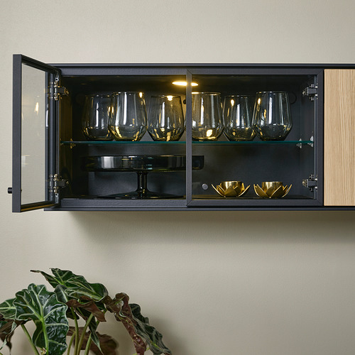 Vitrina de pared con puertas plegables de roble, vitrina y cuencos de oro. La iluminación interior destaca los elementos.