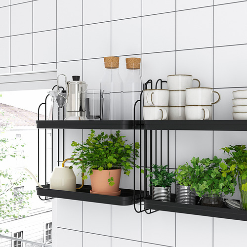 Modern black metal wall shelves hold white mugs, glass jars, and green plants in a white-tiled room, blending style with natural elements.