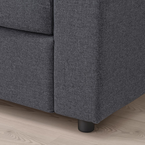Primer plano de un sofá de tela gris oscuro, reposabrazos y patas sobre un suelo de madera.