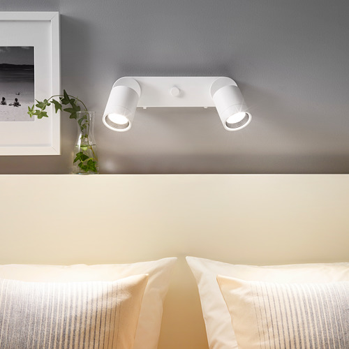 Doble foco NYMÅNE en pared gris sobre la cama, ajustable, con decoración.