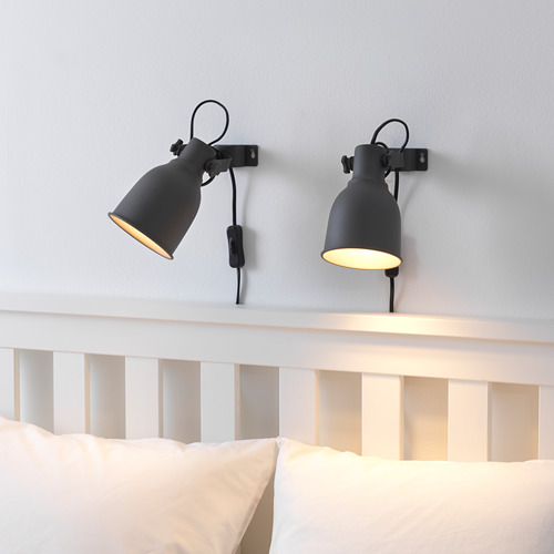 Dos apliques negros ajustables sobre la cama, uno encendido, que ofrecen iluminación de trabajo.