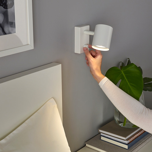 Persona ajustando un interruptor de luz LED regulable montado en la pared cerca de una cabecera y una planta.