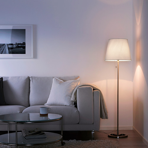 Acogedora sala de estar con lámpara NYFORS, sofá gris y mesa de centro con taza y revistas. Arte sobre el sofá.
