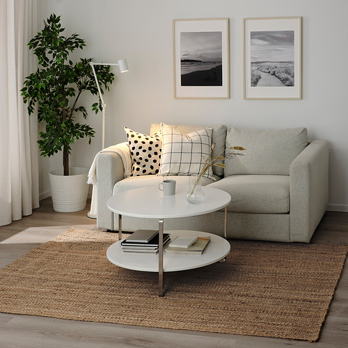 Sala de estar moderna con alfombra STRÖG gris claro, sofá a juego, mesa de centro blanca y fotos enmarcadas en blanco y negro en la pared.