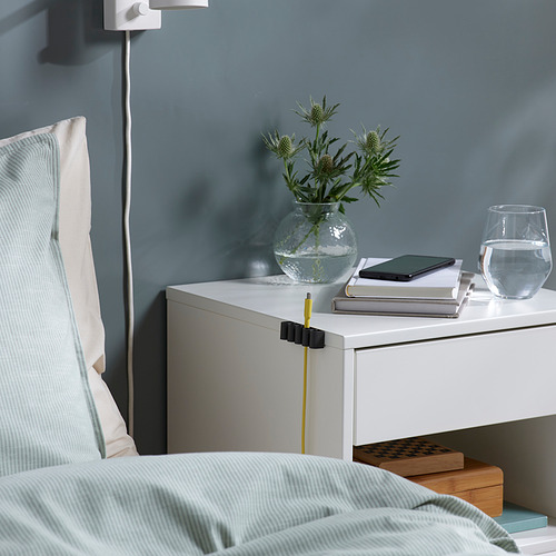 Mesita de noche con cables organizados mediante soportes KALKSTUFF, manteniendo los cables ordenados y accesibles.