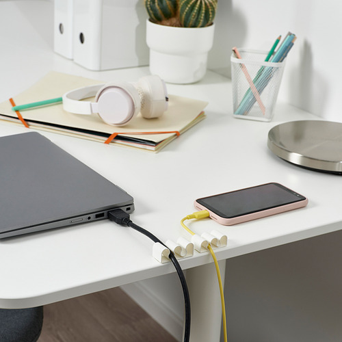 La imagen muestra un escritorio con una computadora portátil, un teléfono inteligente cargando y organizadores de cables KALKSTUFF que mantienen los cables ordenados.