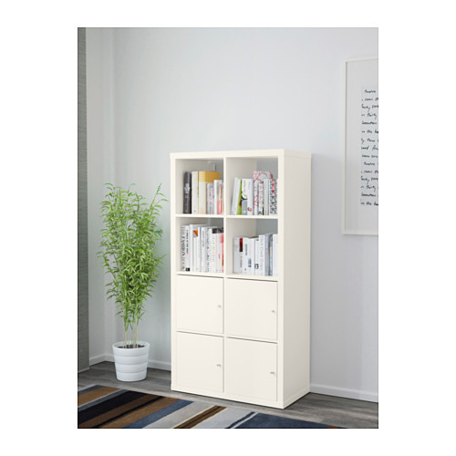 Mueble de almacenaje KALLAX blanco adosado a la pared, sujetando libros. Incluye estantes y armarios cerrados para el almacenamiento. Junto a ella, una gran planta en maceta.
