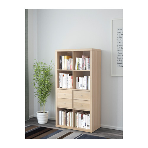 Estantería de madera clara con cajones y libros.