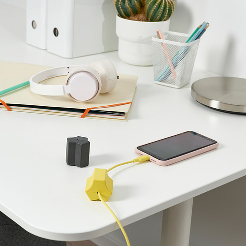 Un espacio de trabajo ordenado con un teléfono que se carga a través de un anclaje usb amarillo HAVSKÅL para mantener el cable ordenado.