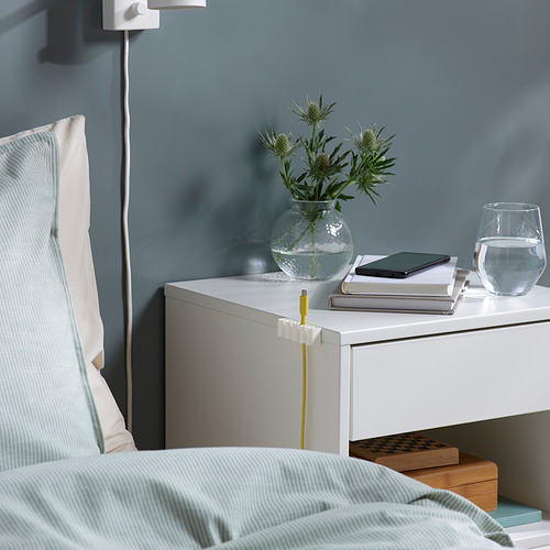 Mesita de noche con cables organizados, mediante soportes KALKSTUFF. Los soportes blancos aseguran los cables, manteniendo el espacio ordenado.